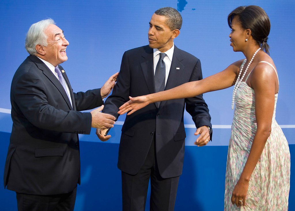 Barack and Michelle Obama speaking at a campaign event, with Barack at a podium and Michelle standing beside him, both expressing enthusiasm and concern for the upcoming election