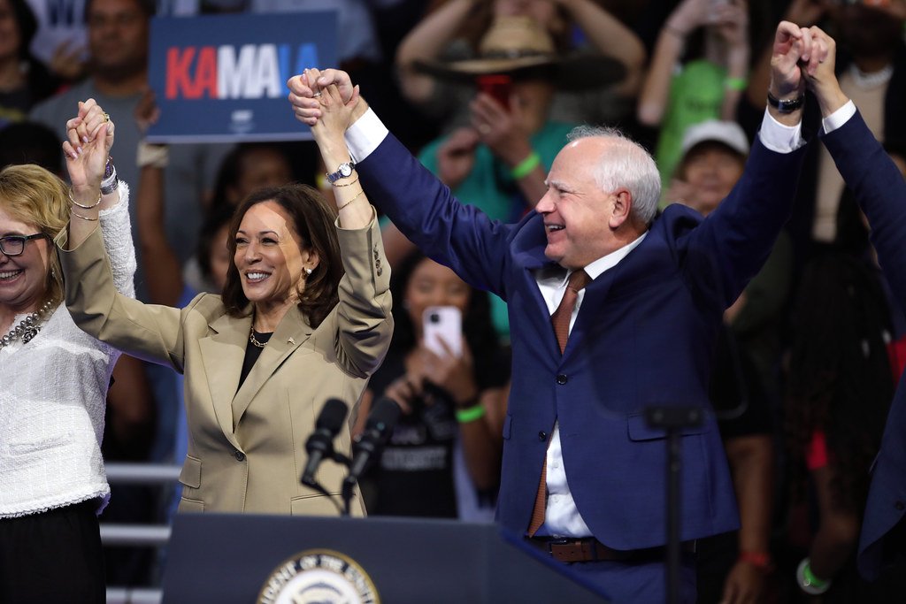 Vice President Kamala Harris and Minnesota Governor Tim Walz on stage at a campaign rally in southern Georgia, with supporters holding signs and banners in the background.